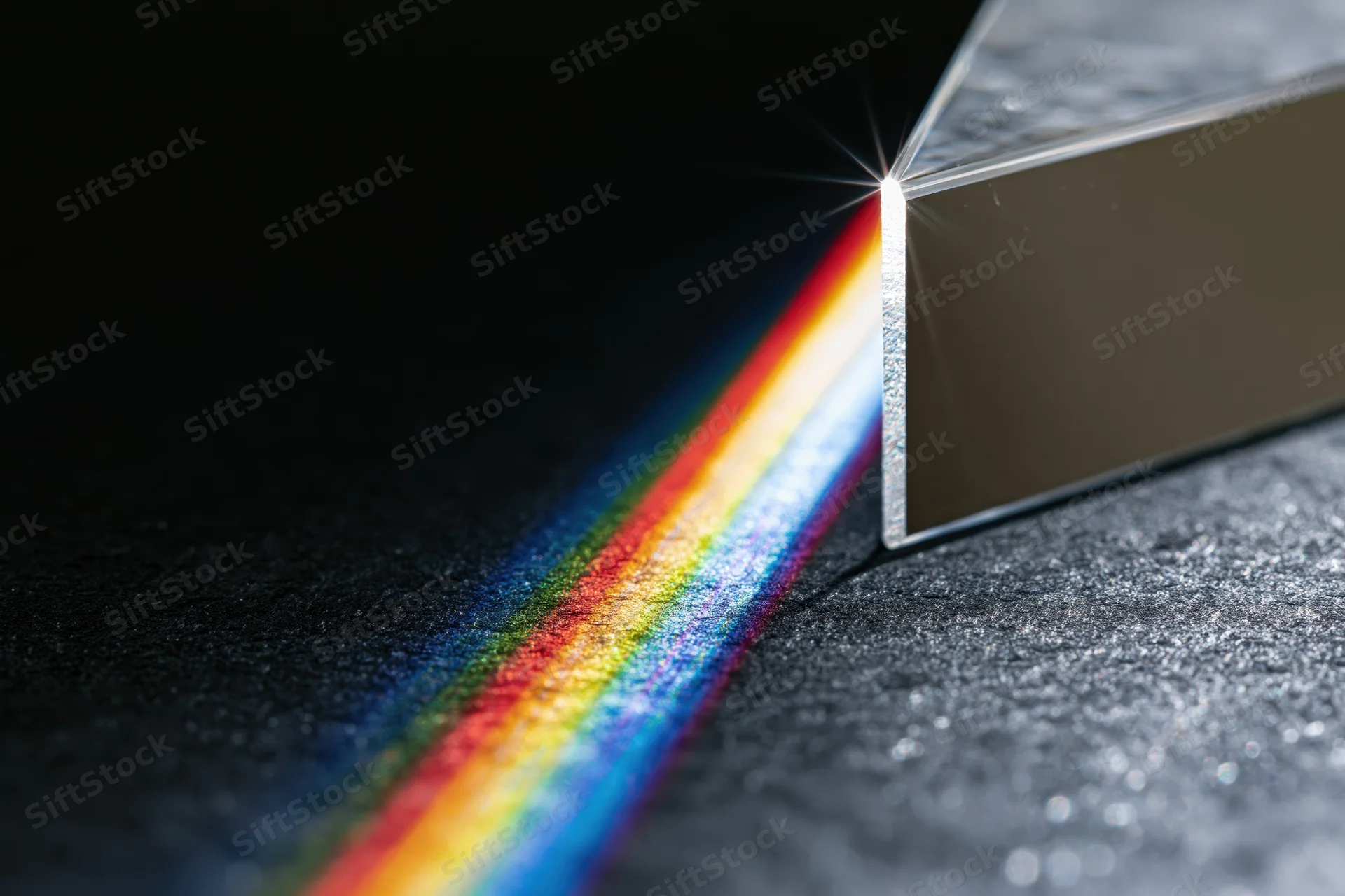 Glass prism refracting a white light beam into a rainbow spectrum on a dark textured surface