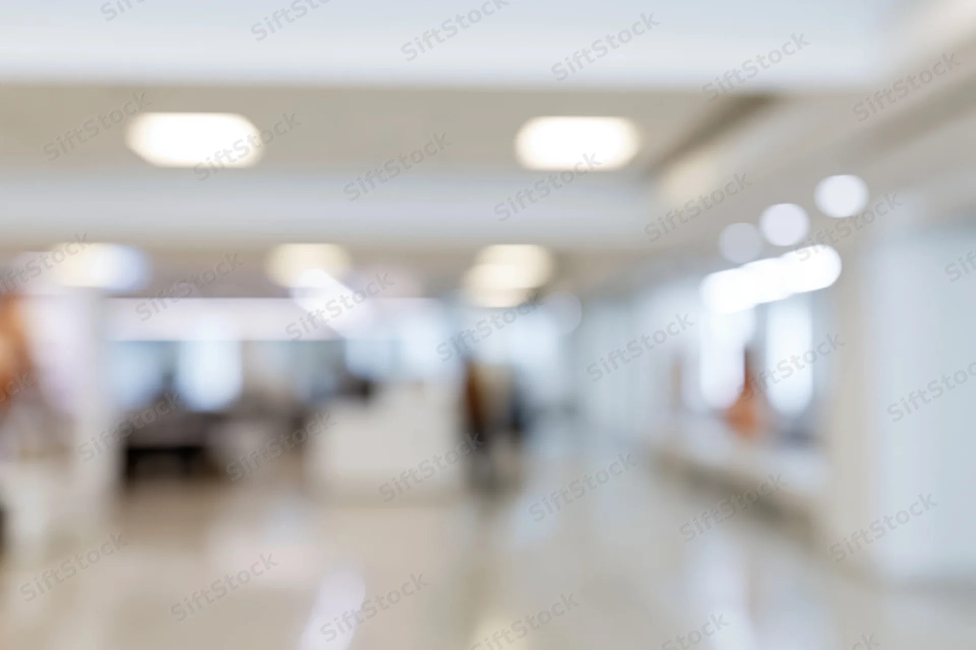 Defocused interior of a bright modern office hallway with ceiling lights and tiled floor
