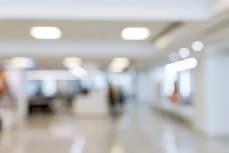 Defocused interior of a bright modern office hallway with ceiling lights and tiled floor