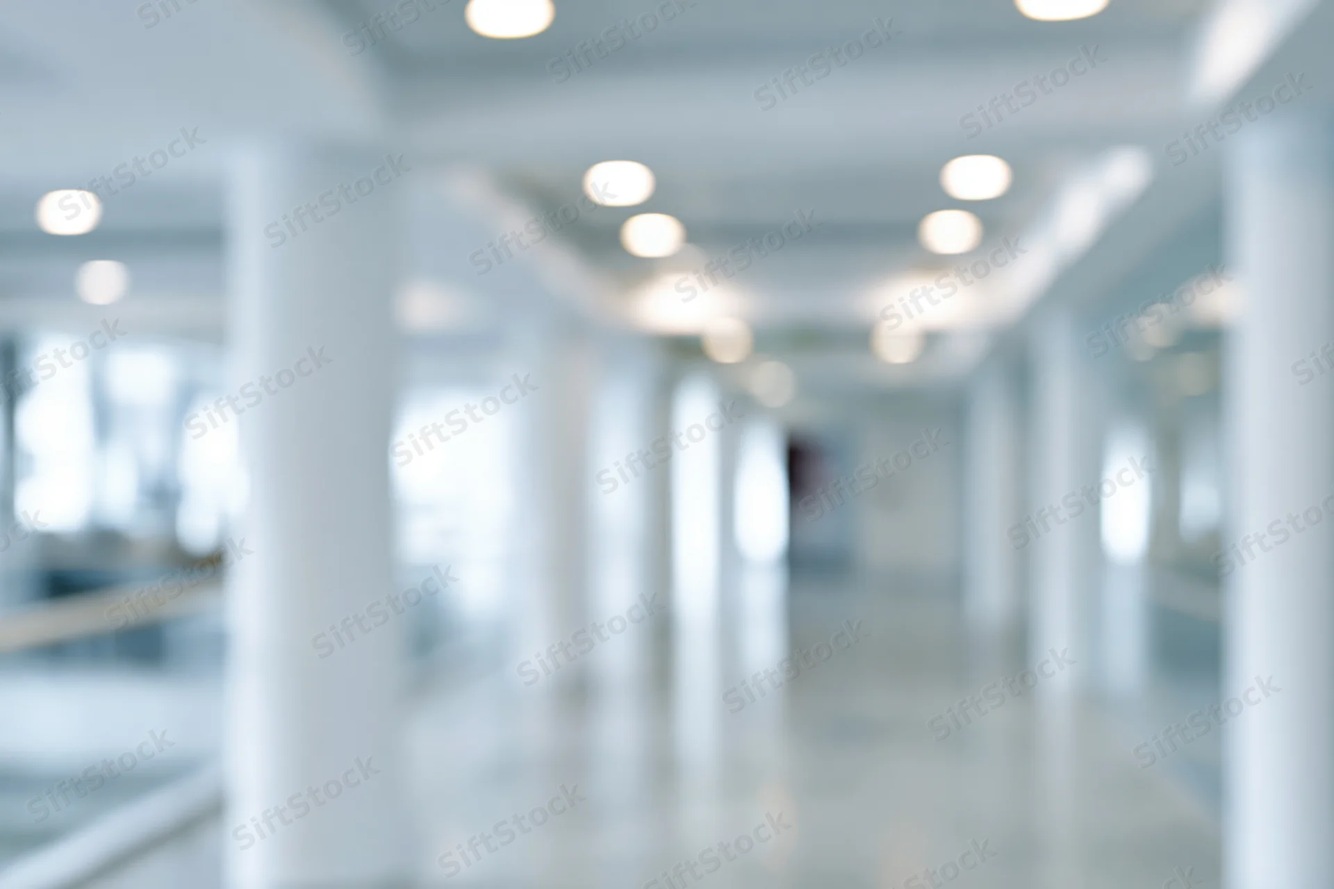 Defocused view of a bright modern office hallway with white columns and recessed ceiling lights