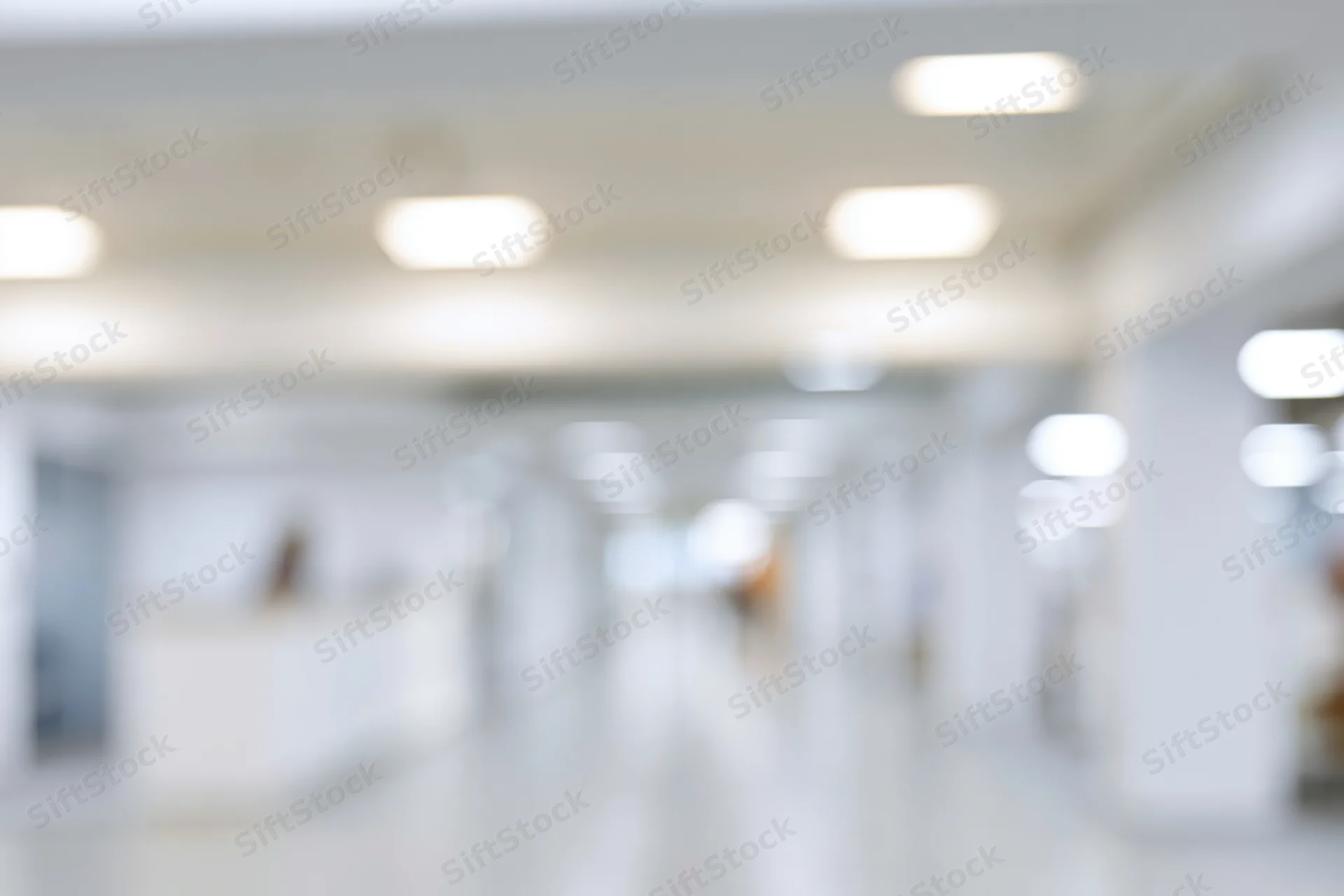 Defocused view of a bright modern office hallway with ceiling lights and white walls