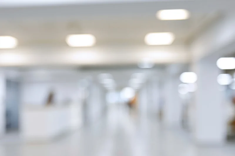 Defocused view of a bright modern office hallway with ceiling lights and white walls