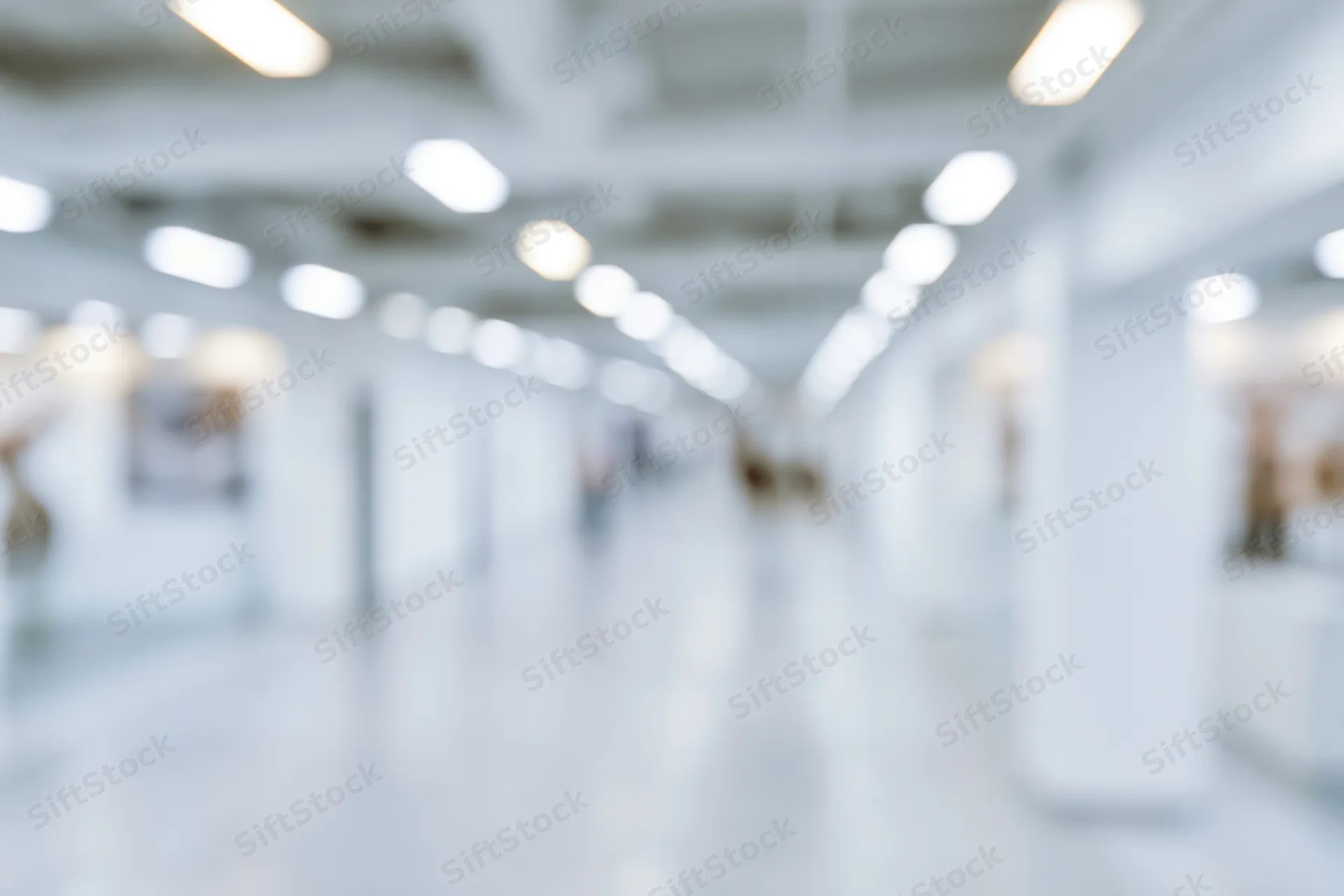 Defocused view of a bright modern office hallway with white pillars and ceiling lights