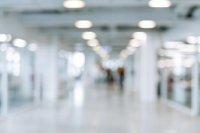 Defocused view of a bright modern office hallway with white columns and glass partitions
