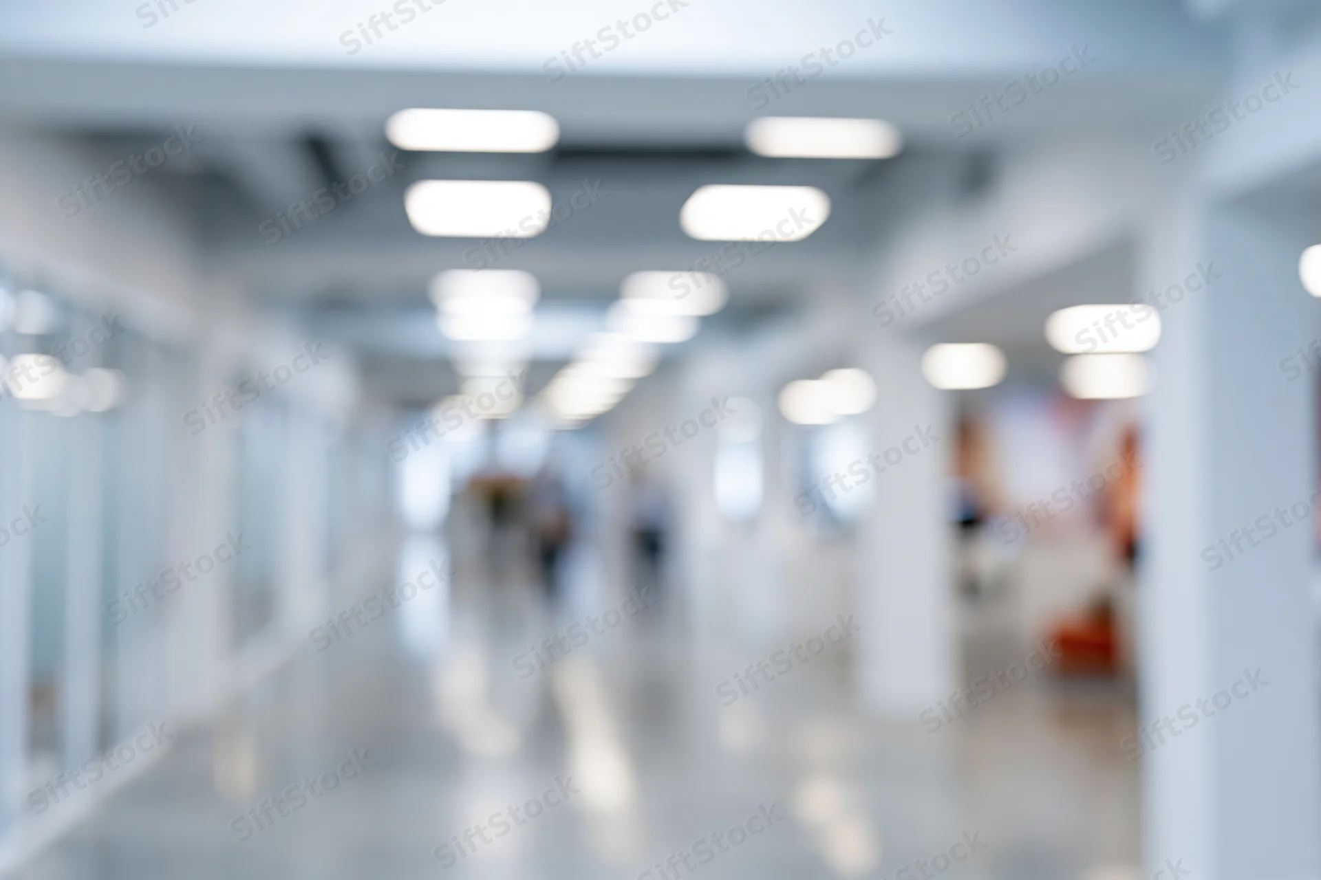 Blurred interior of a modern office hallway with bright ceiling lights and glass partitions