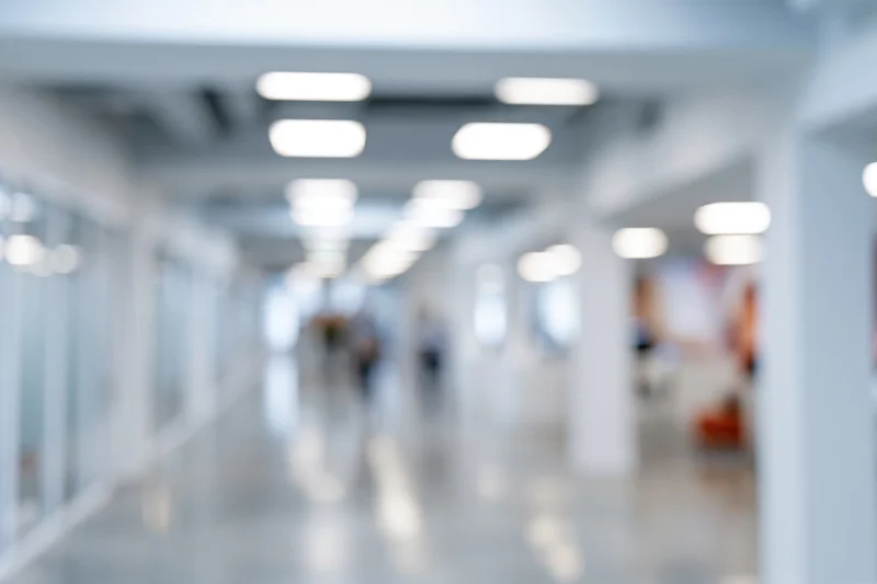 Blurred interior of a modern office hallway with bright ceiling lights and glass partitions
