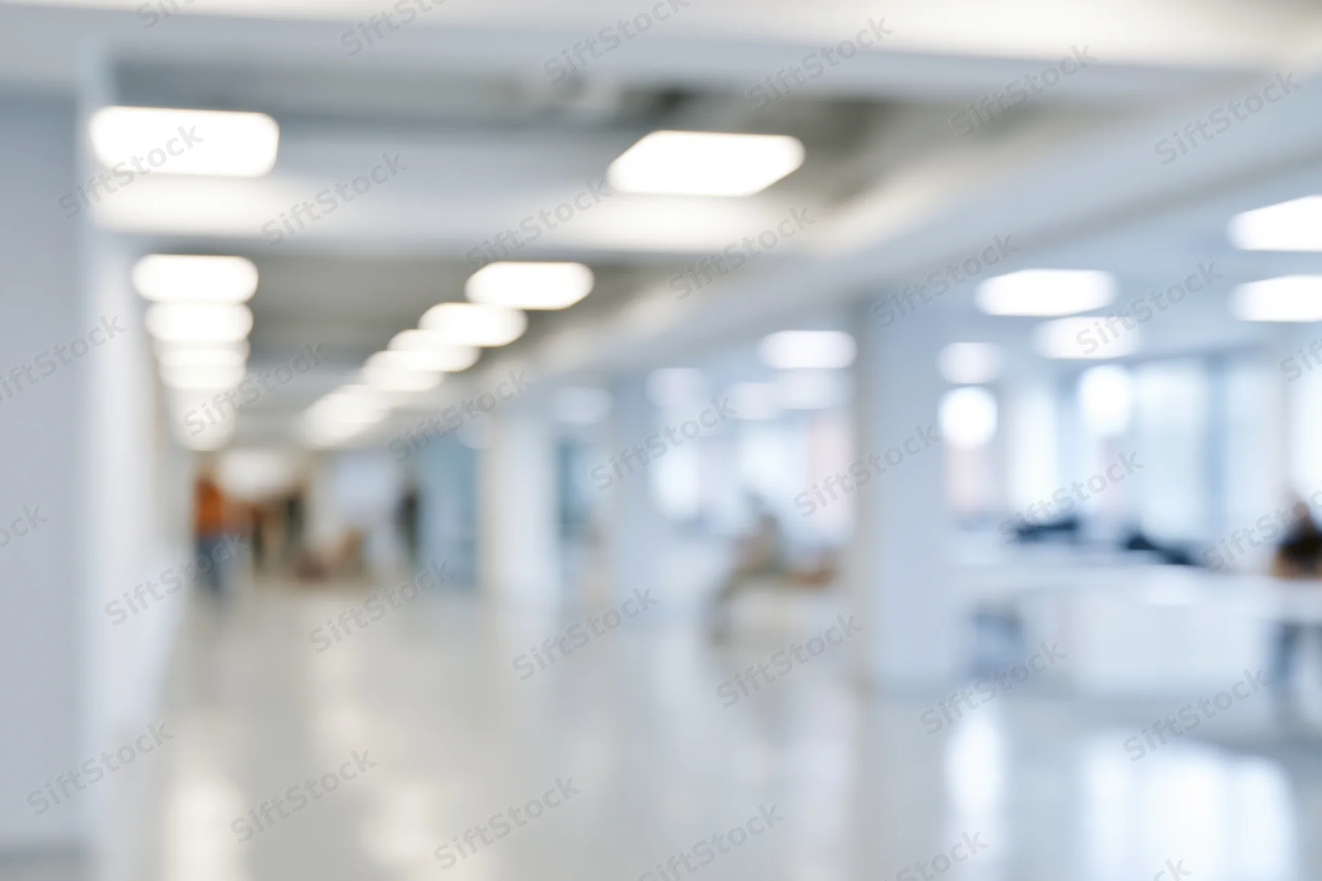 Defocused view of a bright modern office hallway with white walls and ceiling lights