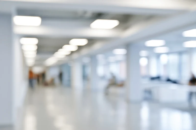 Defocused view of a bright modern office hallway with white walls and ceiling lights