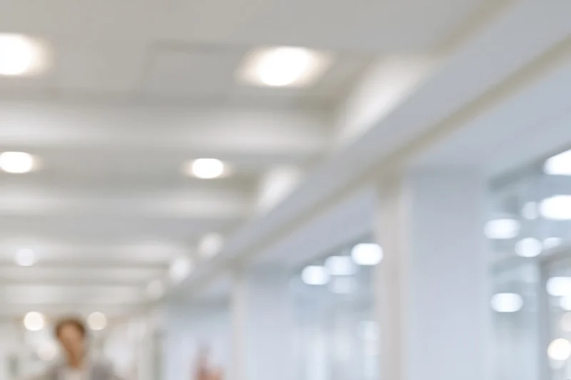 Blurred interior of a bright modern office hallway with recessed ceiling lights and glass partitions