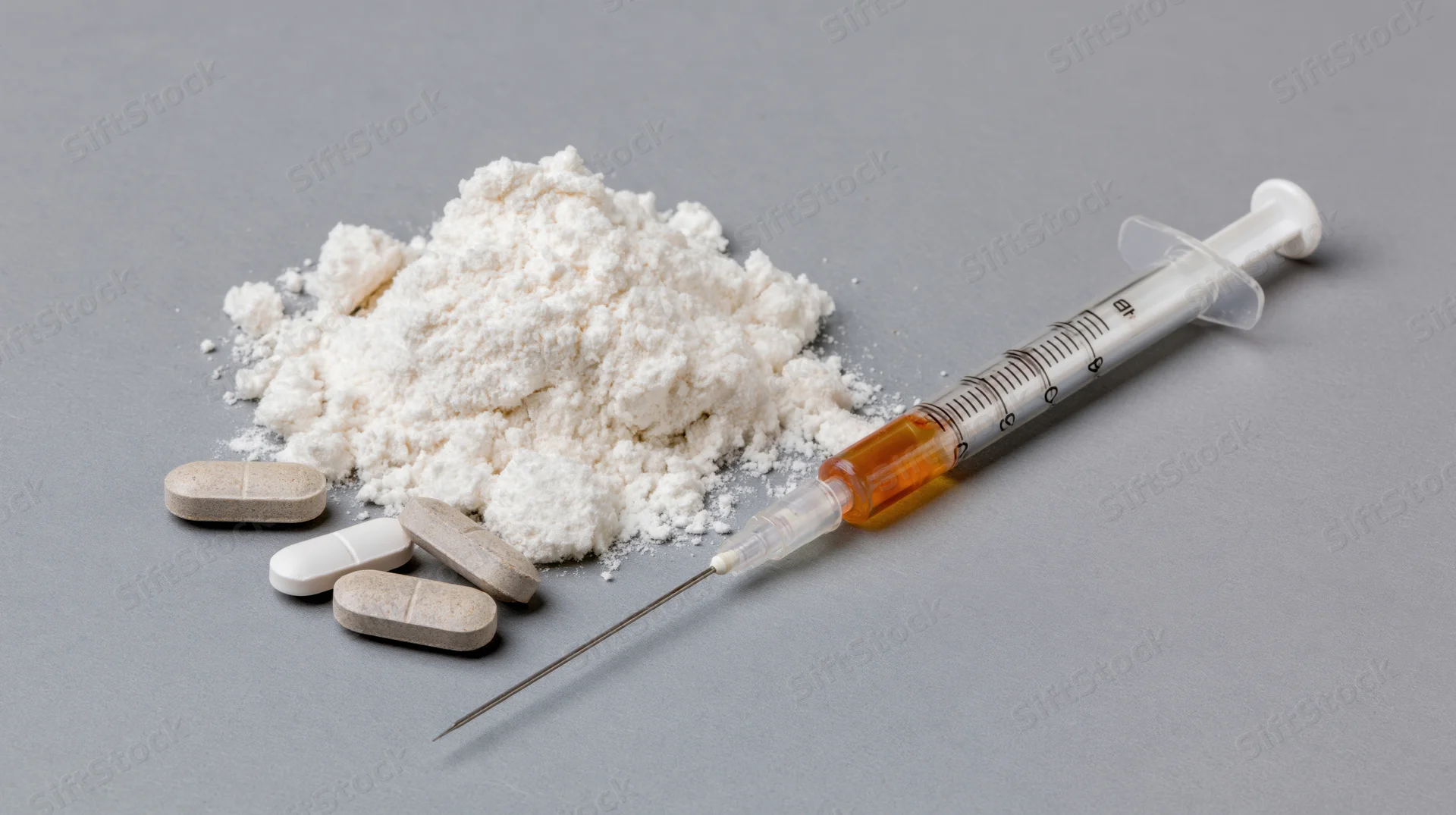 Syringe with orange liquid and white powder alongside pills on gray surface