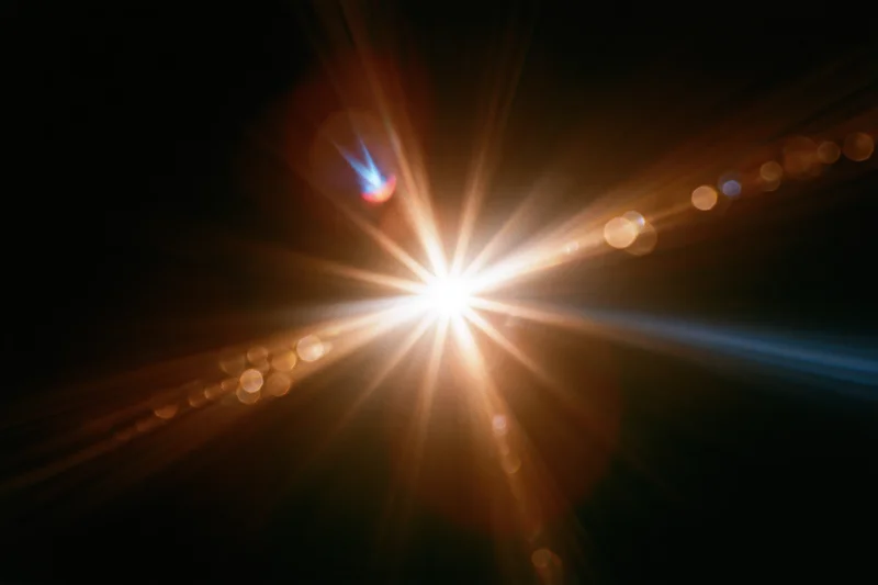 Intense lens flare burst from a single bright point light source in dark background with radiating beams and bokeh circles