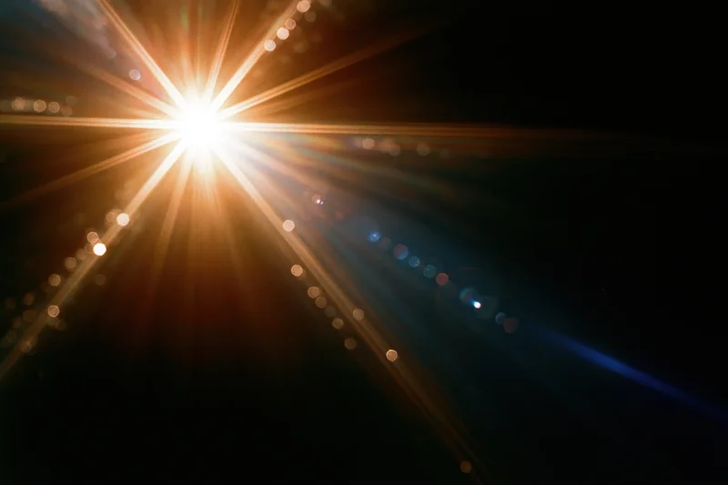 Intense lens flare burst from a single bright point light source in dark space with radiating beams and bokeh circles
