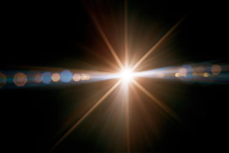 Intense lens flare from a single bright point light source against black background with radial beams and bokeh circles