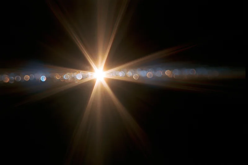Intense lens flare from a single bright light source in dark background with radial beams and bokeh circles
