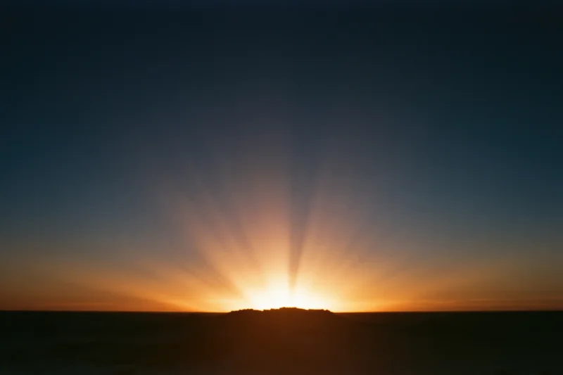 Intense light burst rising from the horizon radiating long sun rays across the sky at dawn
