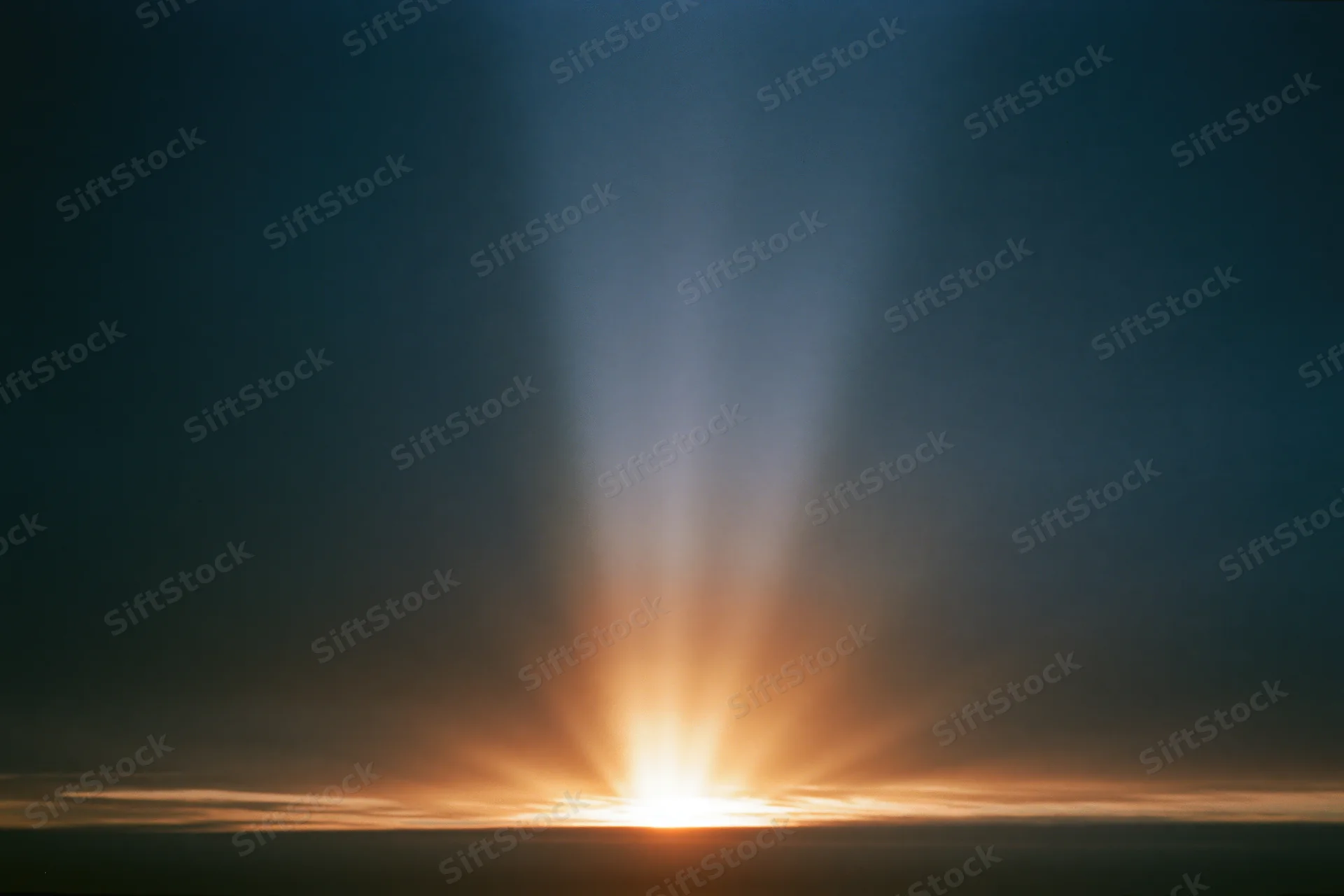 Intense light burst rising from the horizon radiating long sunbeams into the dark sky at dawn