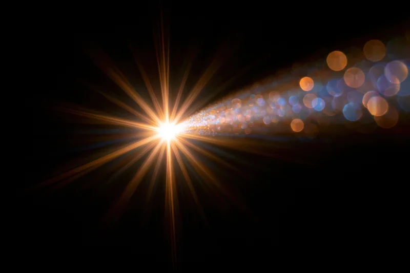 Intense light source emitting starburst rays with bokeh particles against dark background