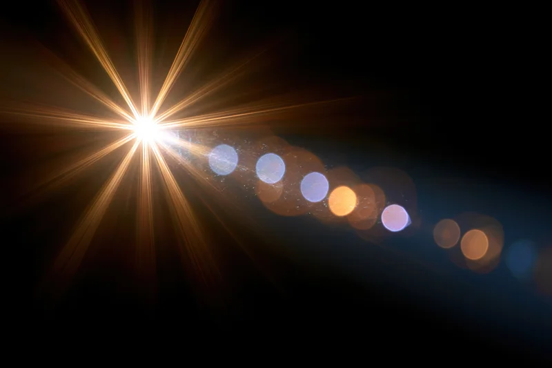 Intense point light source emitting starburst rays with bokeh circles against dark background