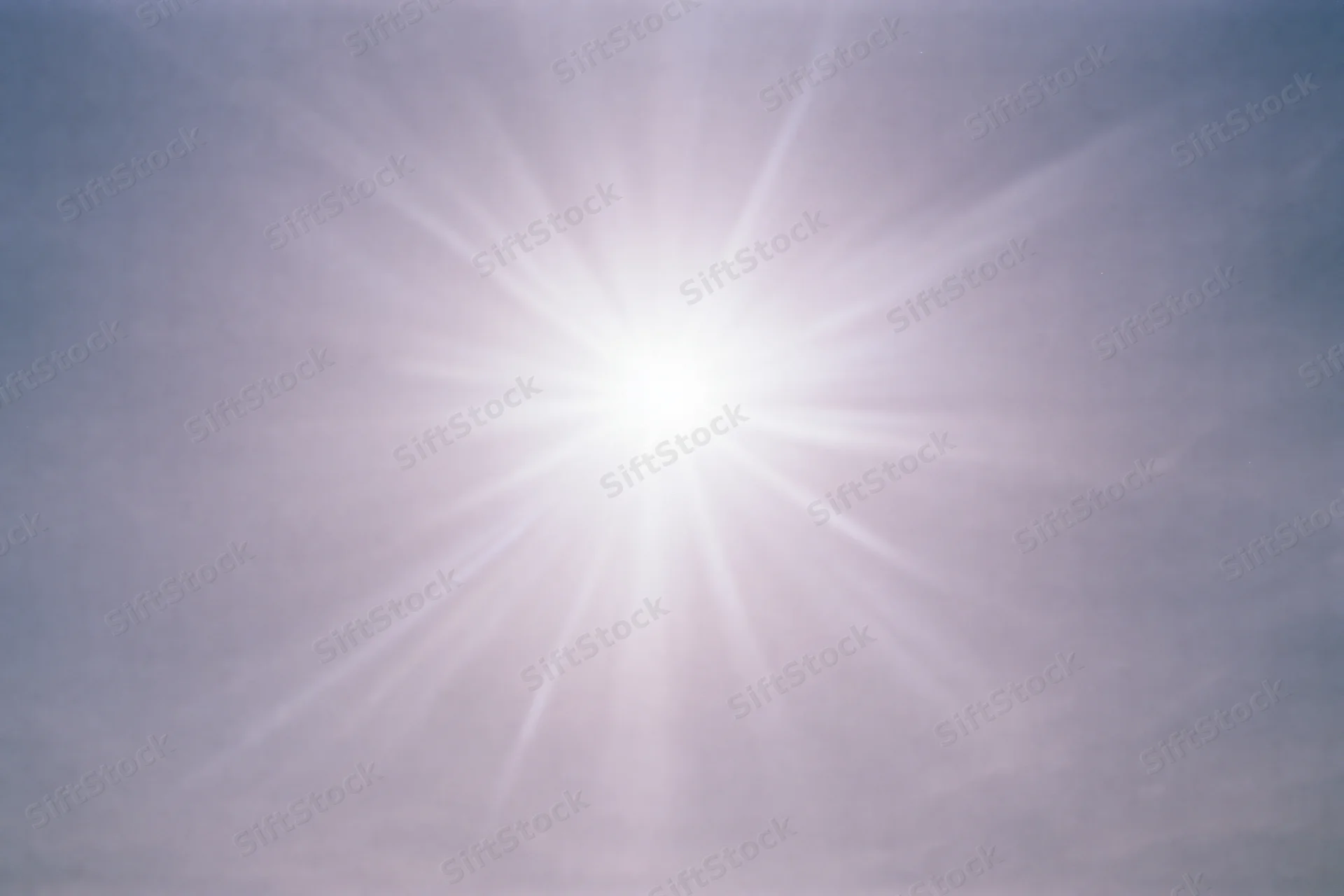 Intense sun flare bursting from upper center of the sky during daytime