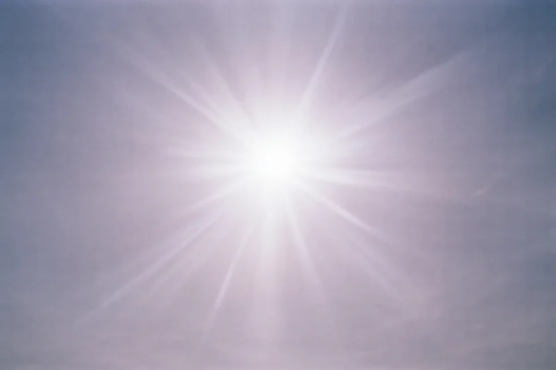 Intense sun flare bursting from upper center of the sky during daytime