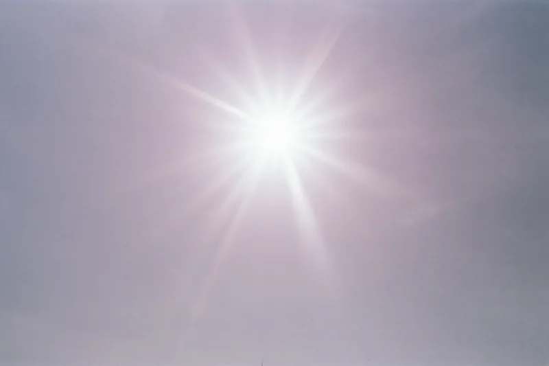Intense sun flare bursting from upper center of the sky against a clear bright background