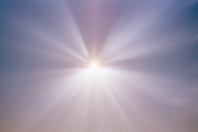 Intense sun flare bursting from upper center of frame against hazy sky