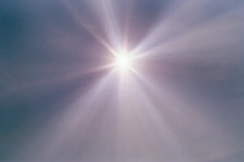 Intense sun flare bursting from upper center of frame against blue sky