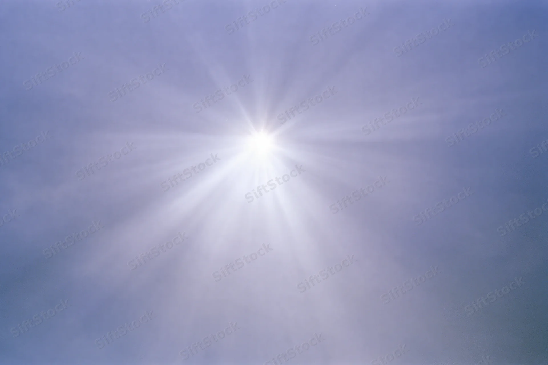 Intense sun flare bursting from upper center of frame against blue sky
