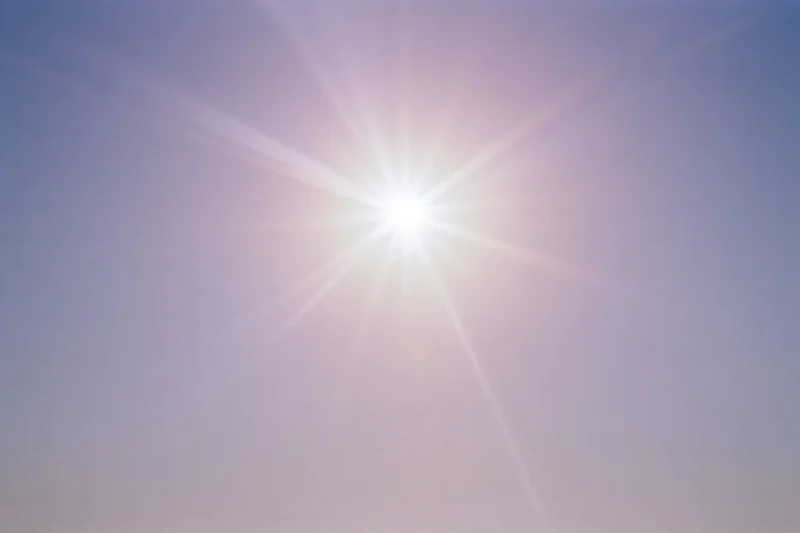 Intense sun flare bursting from upper center of frame against clear sky