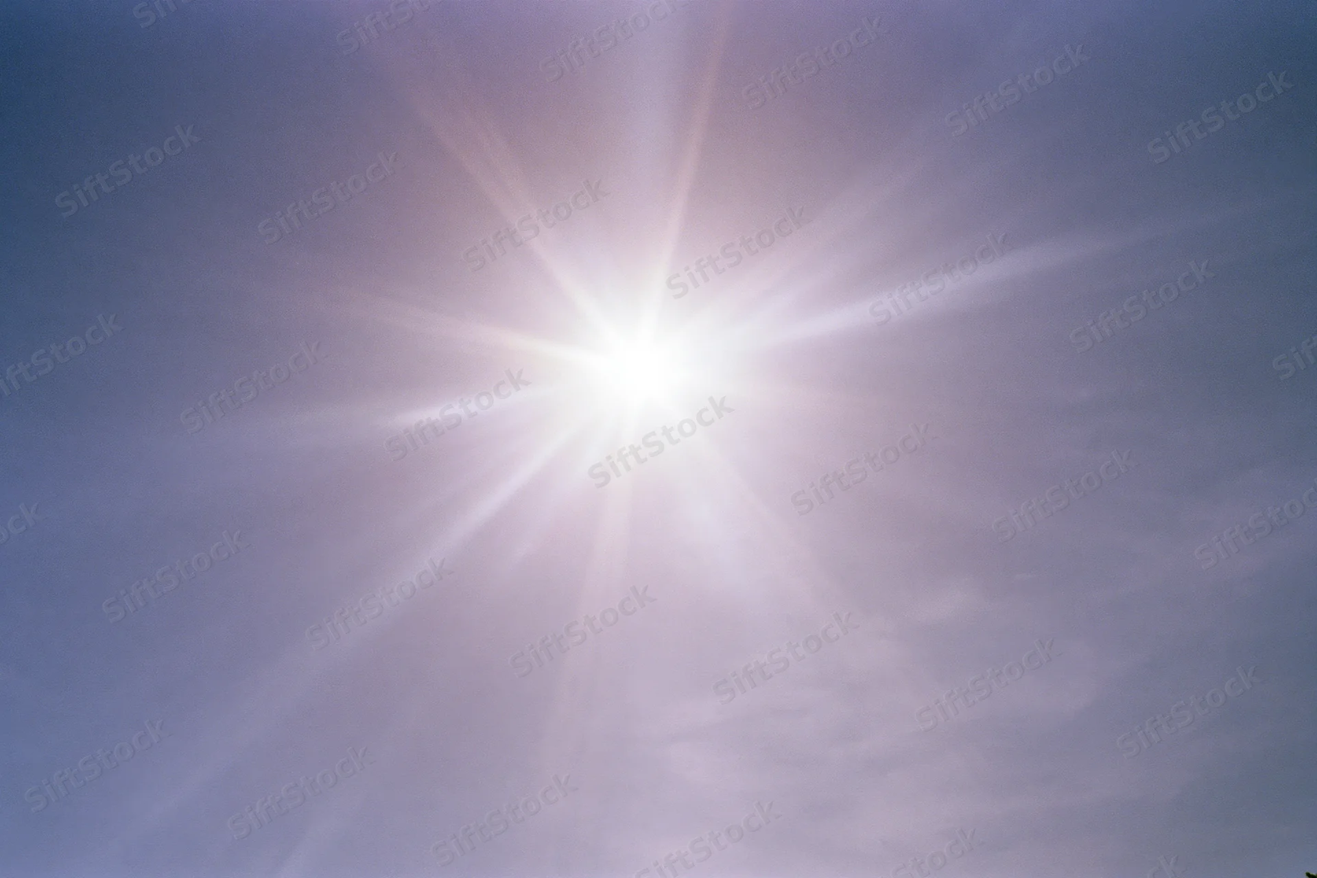 Intense sun flare bursting from upper center of frame against clear blue sky