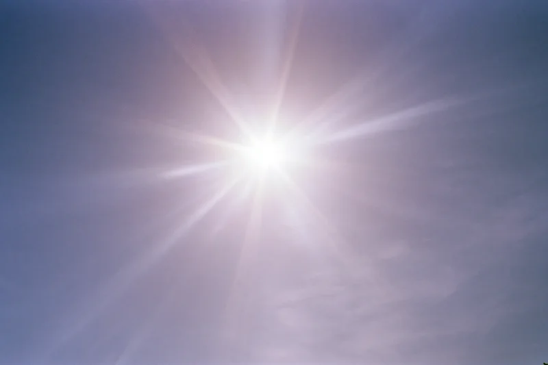 Intense sun flare bursting from upper center of frame against clear blue sky