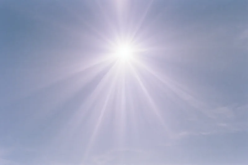 Intense sunburst radiating from upper center of clear blue sky