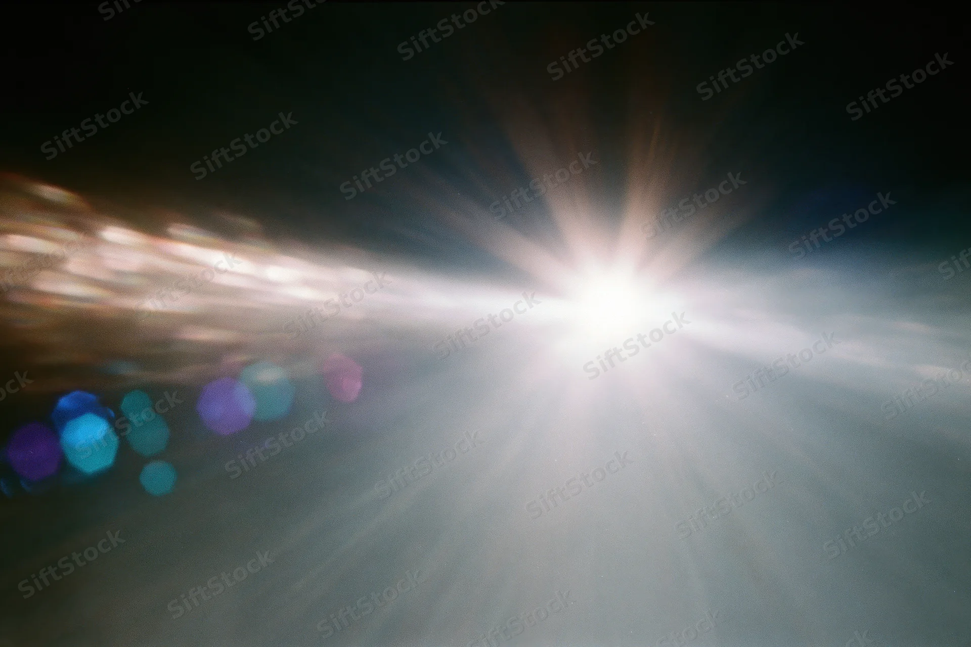 Intense white light source blazing against a near-black background with colorful bokeh and lens flare effects