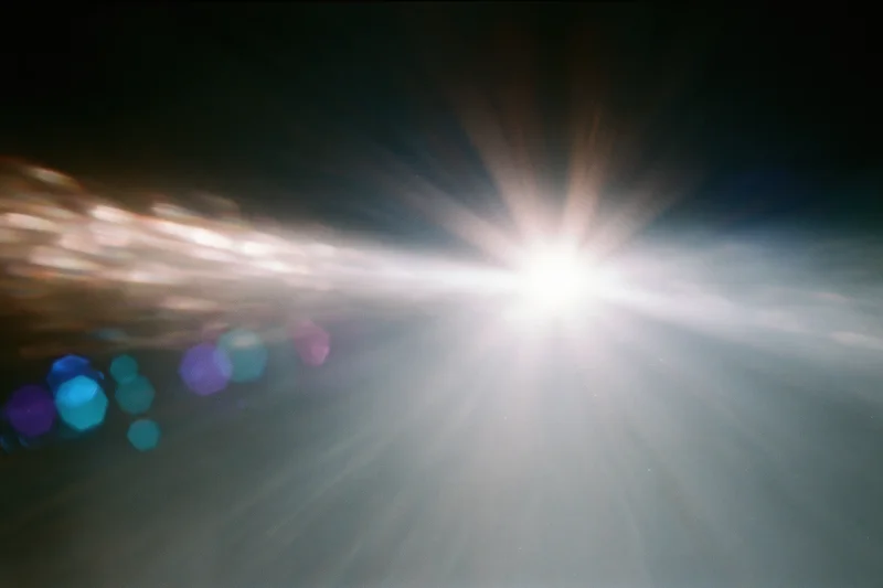 Intense white light source blazing against a near-black background with colorful bokeh and lens flare effects