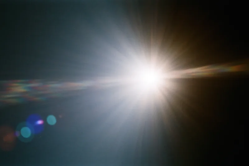 Intense white light source blazing against a near-black background with lens flare and rainbow streaks
