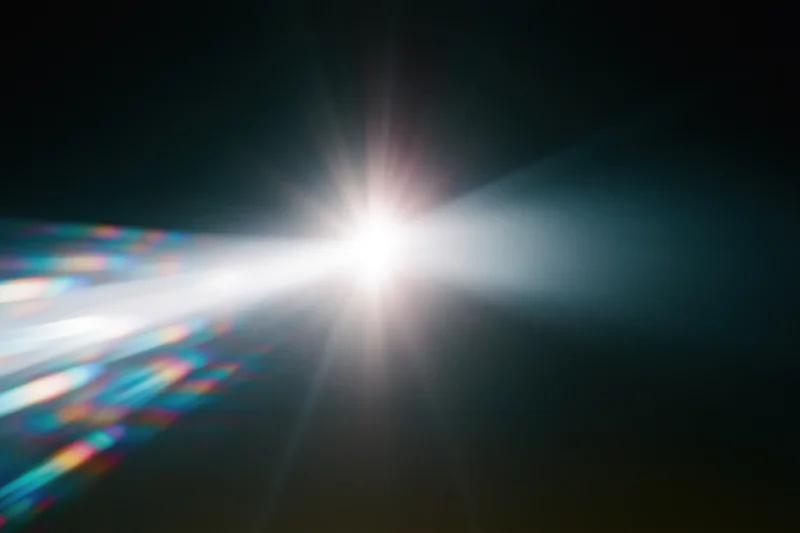 Intense white light source blazing against a near-black background with colorful lens flare and starburst effect