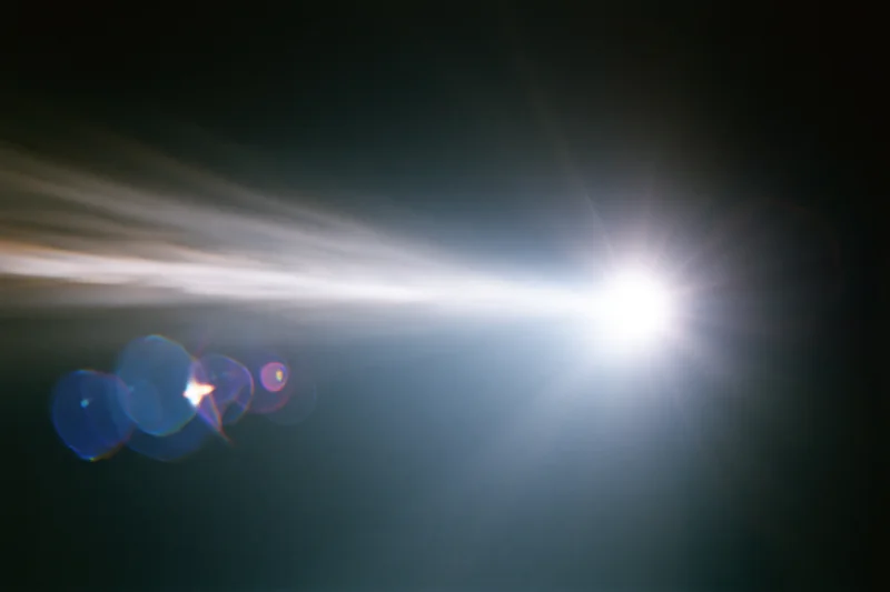 Intense white light source blazing against a near-black background with lens flare and bokeh effects