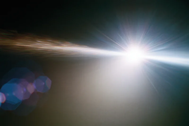 Intense white light source blazing against a near-black background with lens flare and bokeh effects