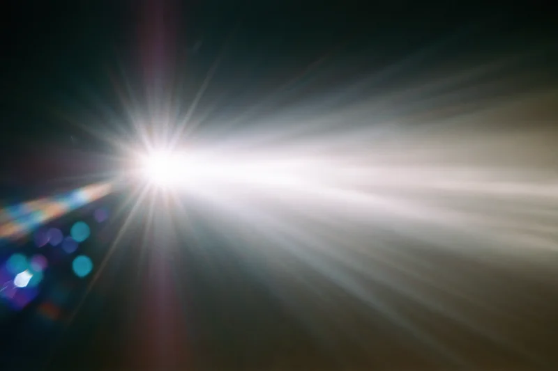 Intense white light source radiating beams against dark background with colorful bokeh highlights