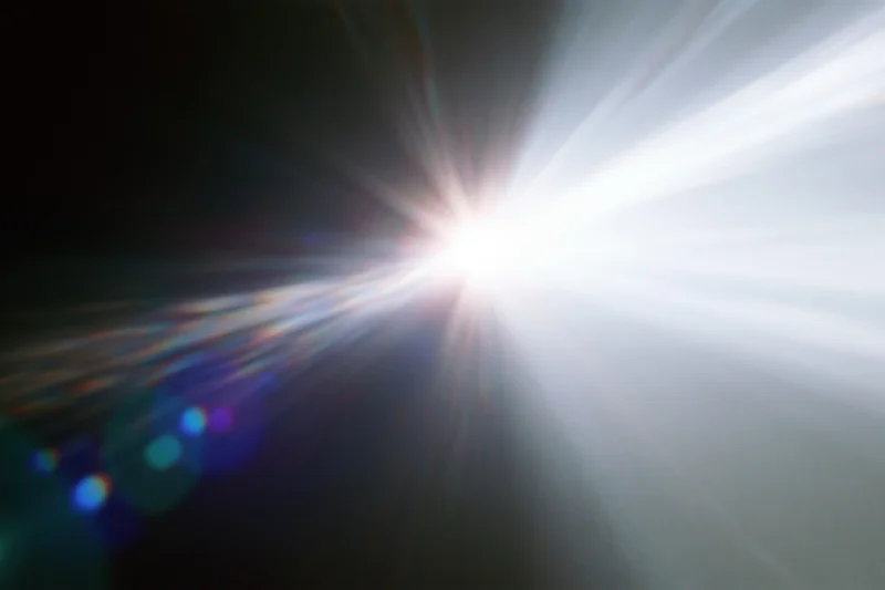Intense white light source radiating bright beams against dark background with lens flare and bokeh effects