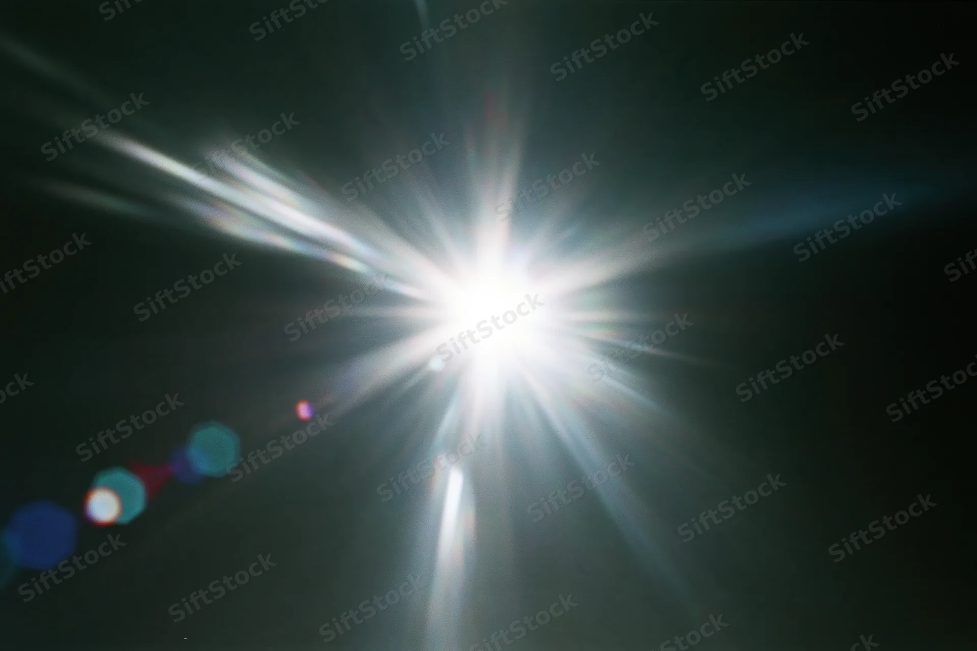 Intense white light source radiating bright beams against dark background with lens flare and bokeh effects