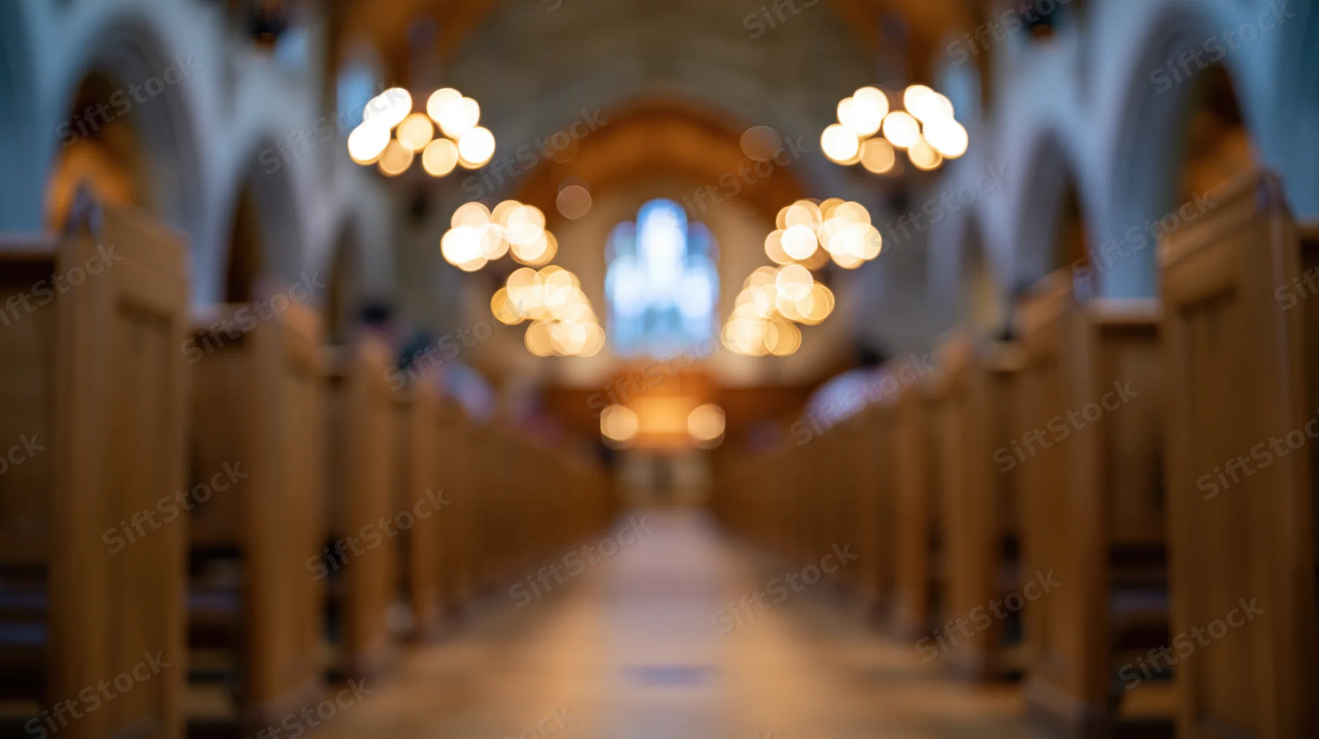 Central aisle of a church nave lined with wooden pews leading to a stained glass window at the altar