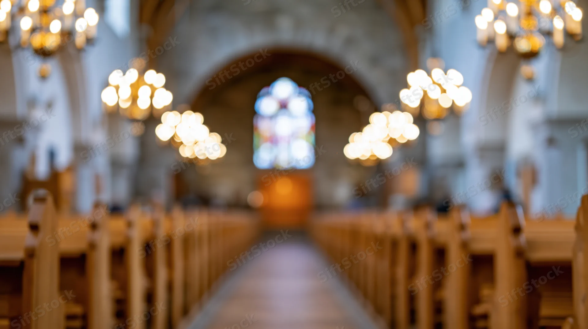 Central aisle of a church nave lined with wooden pews leading to a stained glass window at the altar