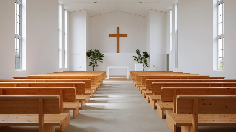 Empty wooden pews arranged in rows facing a white altar with a wooden cross in a minimalist modern church sanctuary