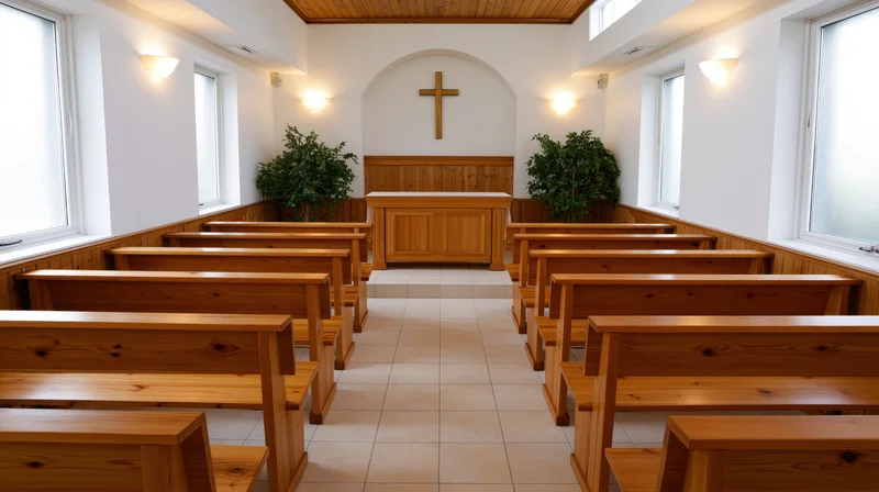 Empty wooden pews arranged in rows inside a small protestant chapel with a cross above the altar