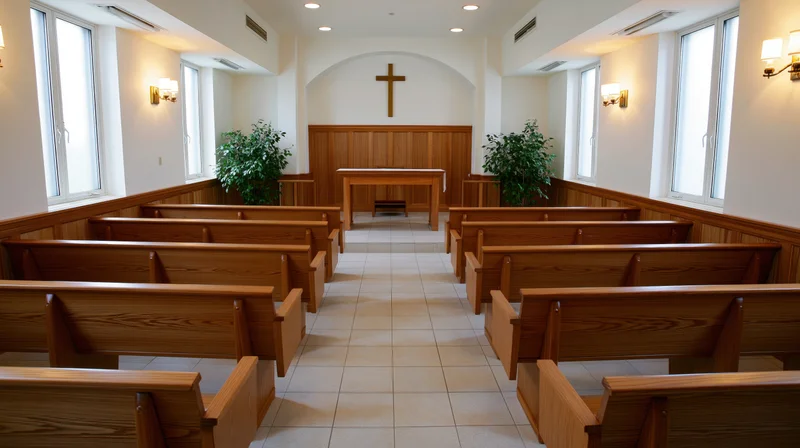 Empty wooden pews arranged in rows facing an altar with a cross in a small protestant chapel interior