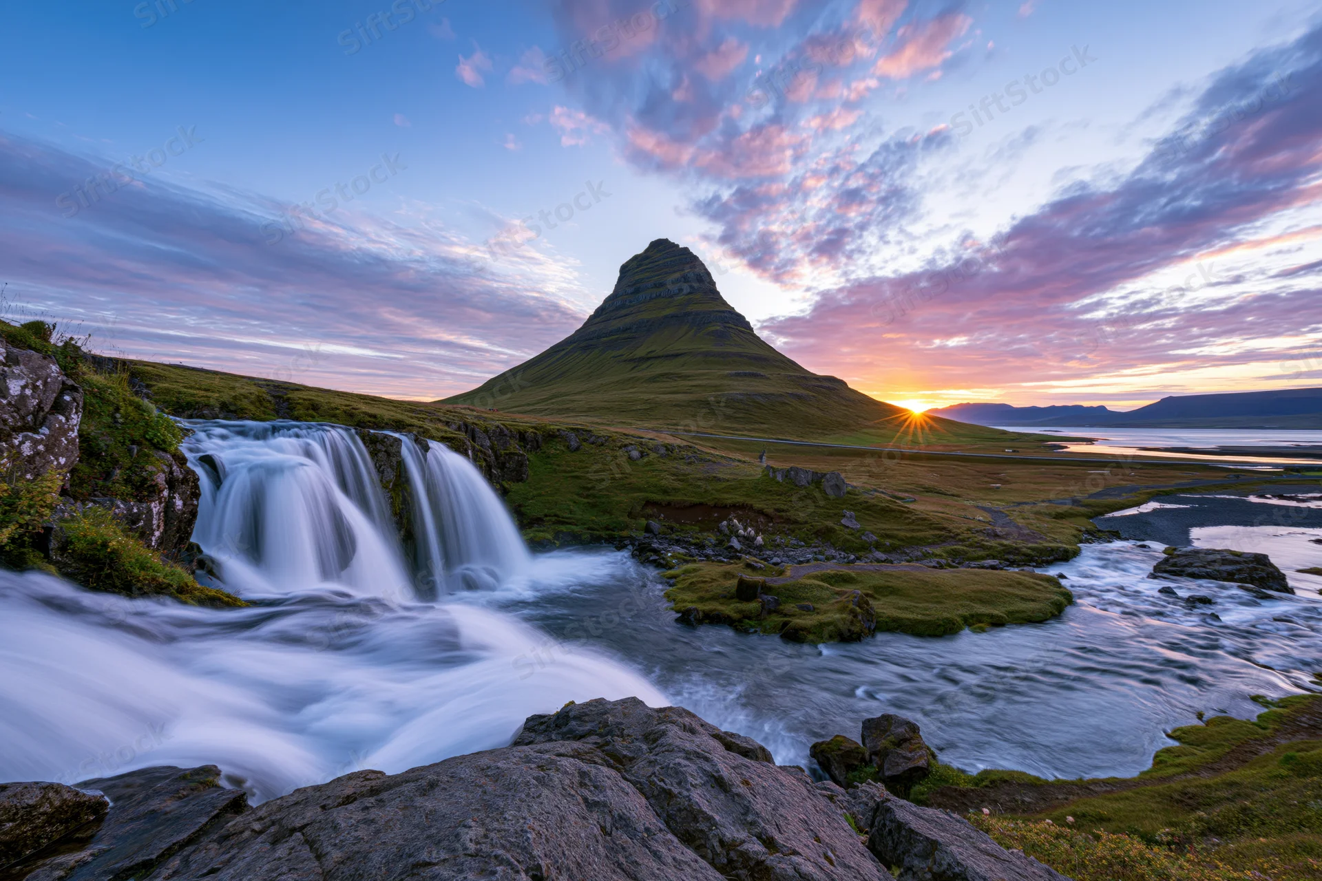 Kirkjufell mountain rising above a cascading waterfall at sunset in iceland