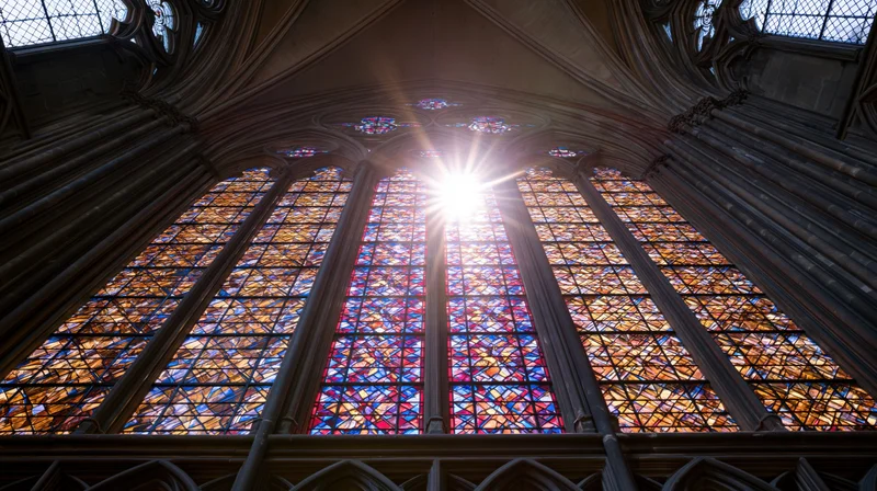 Large gothic stained glass cathedral window viewed from below with sunlight streaming through