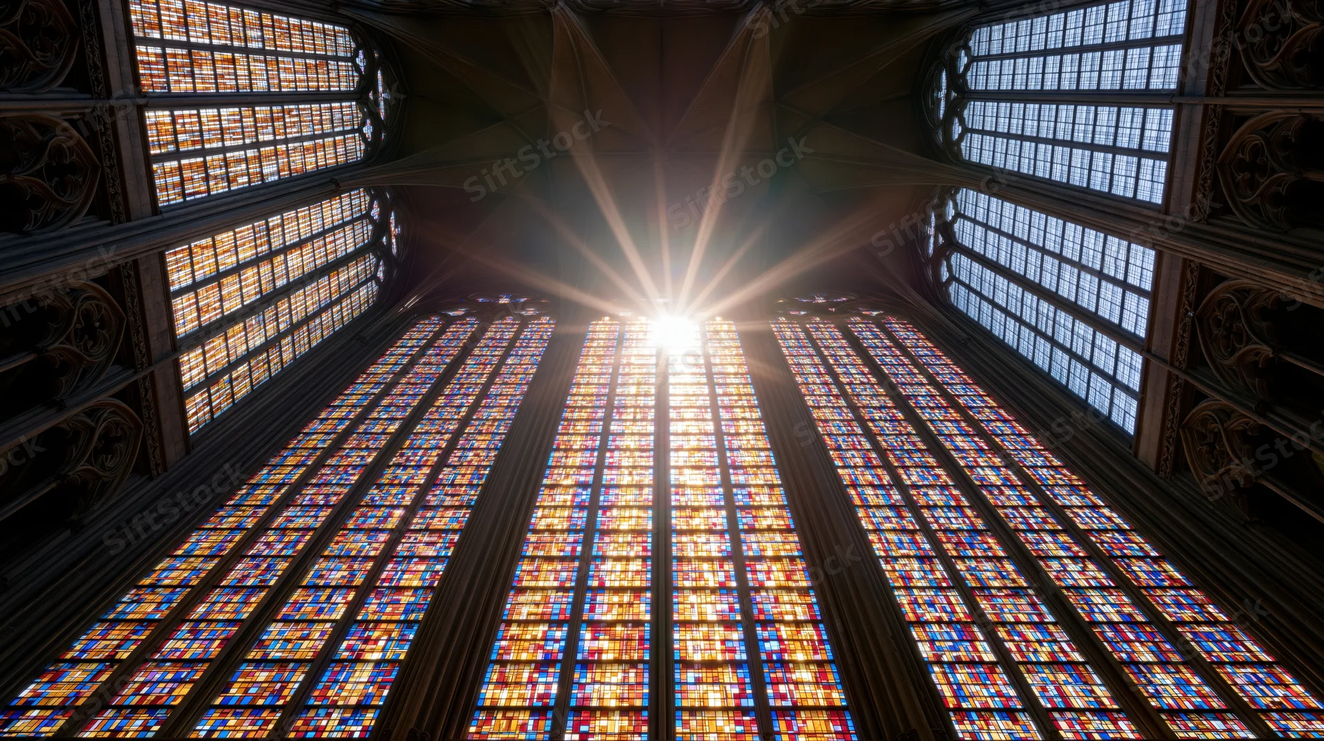Large gothic stained glass window viewed from below inside a cathedral interior