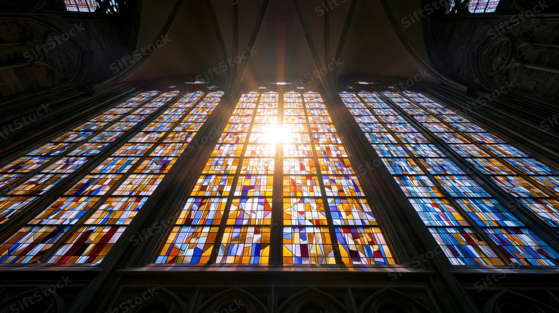 Large gothic stained glass cathedral window viewed from below with sunlight streaming through